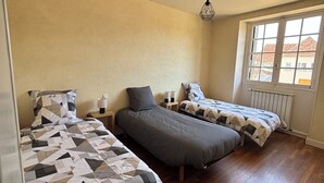 Een kamer met drie op een rij staande bedden, houten vloeren, een raam met uitzicht en een hanglamp.