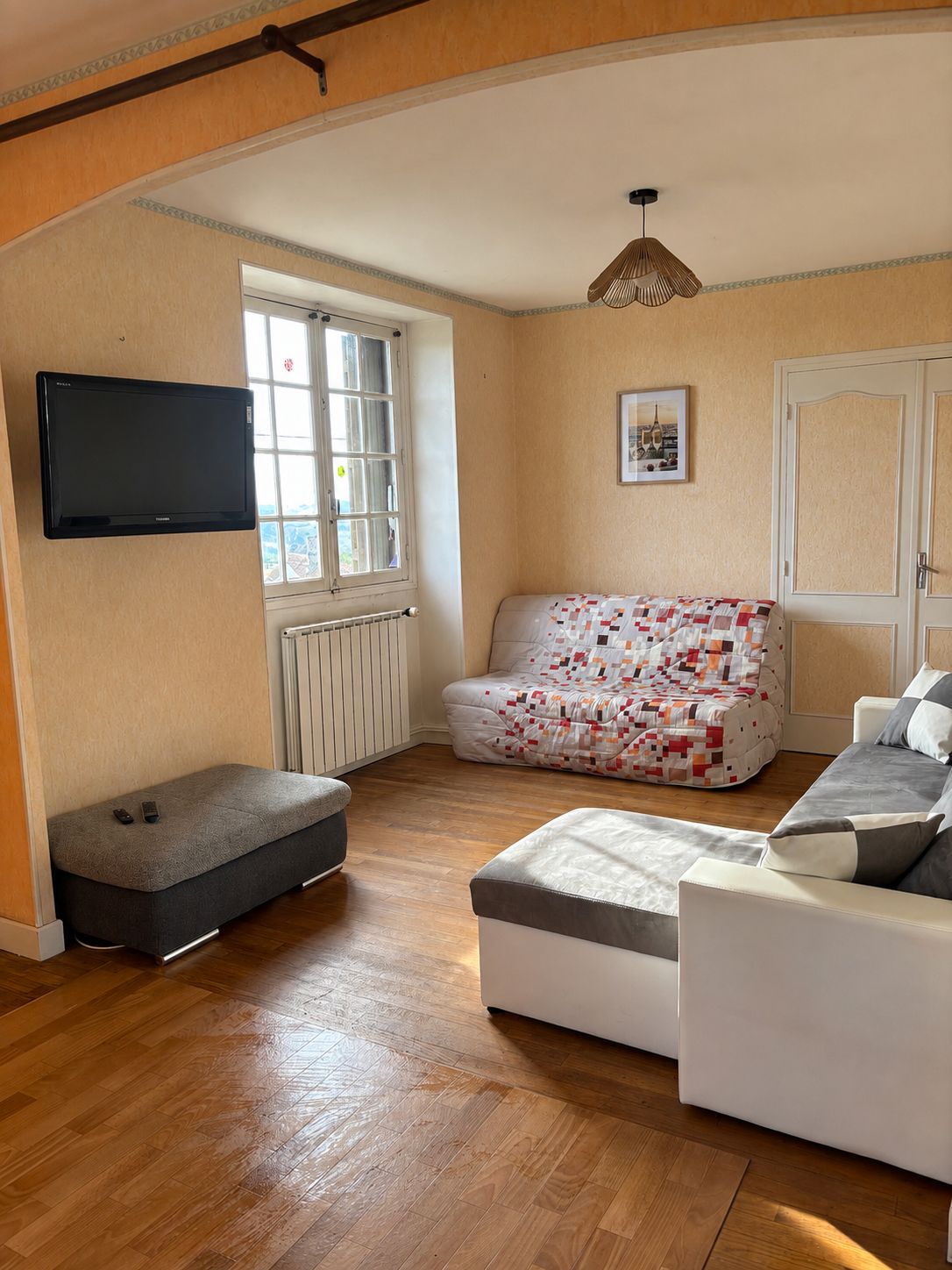 Sala de estar com sofá, um banquinho e uma TV de tela plana fixada na parede.