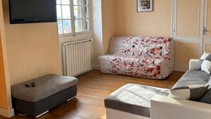 Een woonkamer met een bank, een poef en een flatscreen televisie aan de muur.