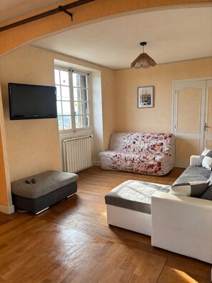 Ein Wohnzimmer mit einer Couch, einem Hocker und einem flachbildfernseher an der Wand.