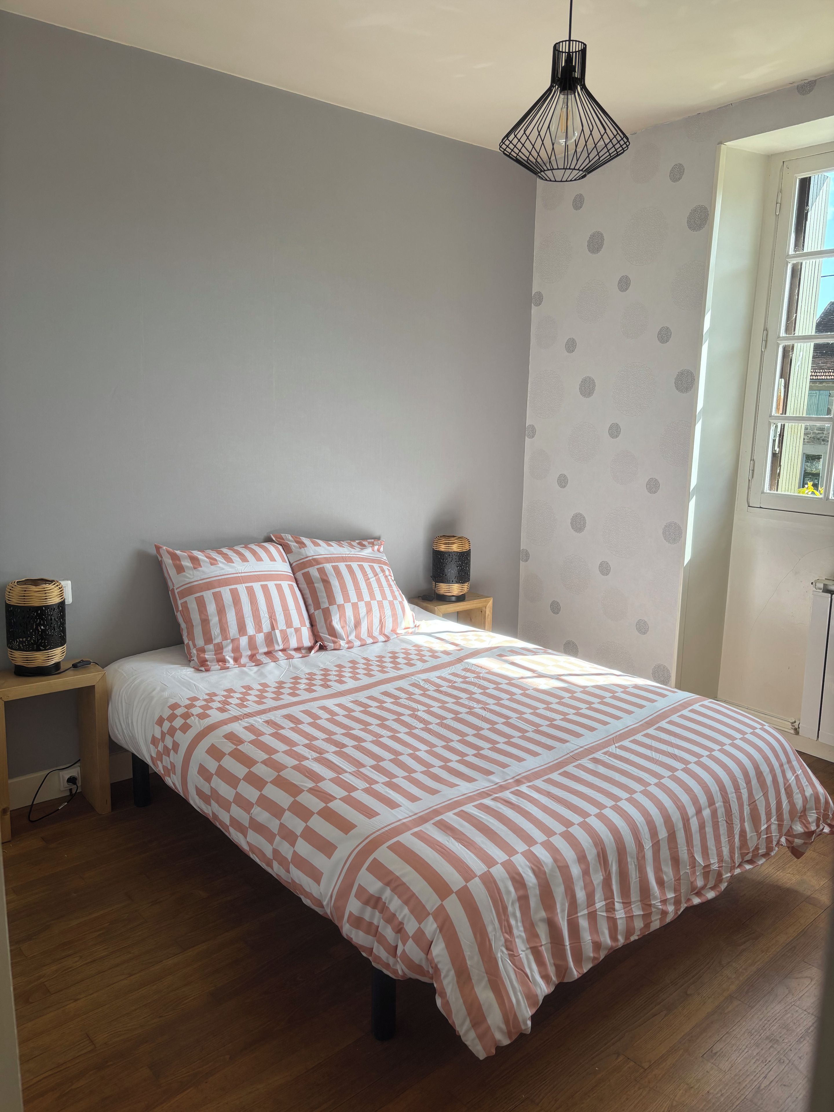 A bedroom with a bed, a bedside table, a lamp, and a window.