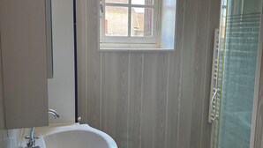Een badkamer met een wit wastafel, een spiegel, een raam en een douchehoek.