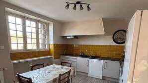 Een kleine keuken met een eettafel, witte kastjes, een ingebouwde oven en een klok aan de muur.