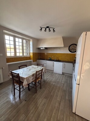 Eine kompakte Küche mit Esstisch, weißen Schränken, einem eingebauten Backofen und einer Uhr an der Wand.