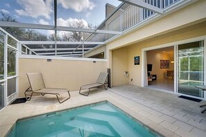 Ein moderner Poolbereich im Freien mit zwei Liegestühlen, einer glasgeschlossenen Terrasse und Blick auf die umliegende Landschaft.