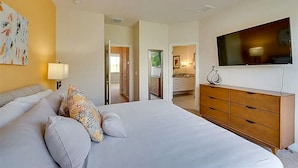Quarto de hotel com cama, penteadeira, televisão e um quadro na parede.