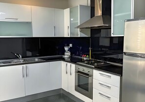 A modern kitchen with white cabinets, a black countertop, a stove, and a refrigerator. - Perfect Landing Pad (Gouvernorat de l'Ariana)