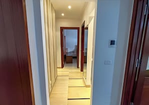 A hallway with wooden doors, a light switch, and a thermostat on the wall. - Perfect Landing Pad (Gouvernorat de l'Ariana)