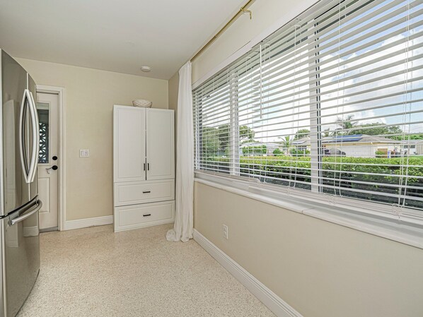 A kitchen with a refrigerator, a white cabinet, and a window with blinds.