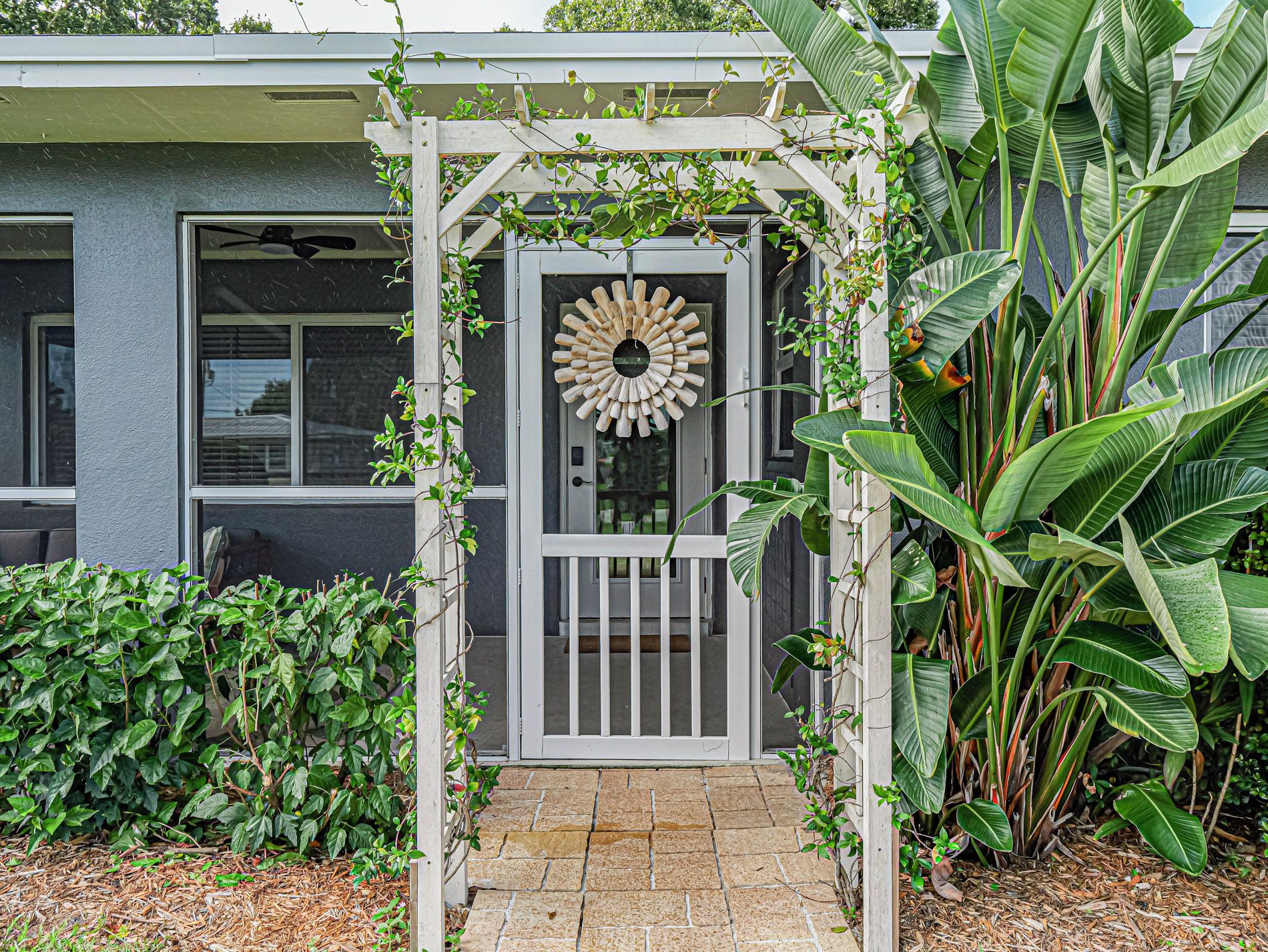 Een huisentree met een houten pergola, een decoratieve deurklopper en weelderige beplanting.