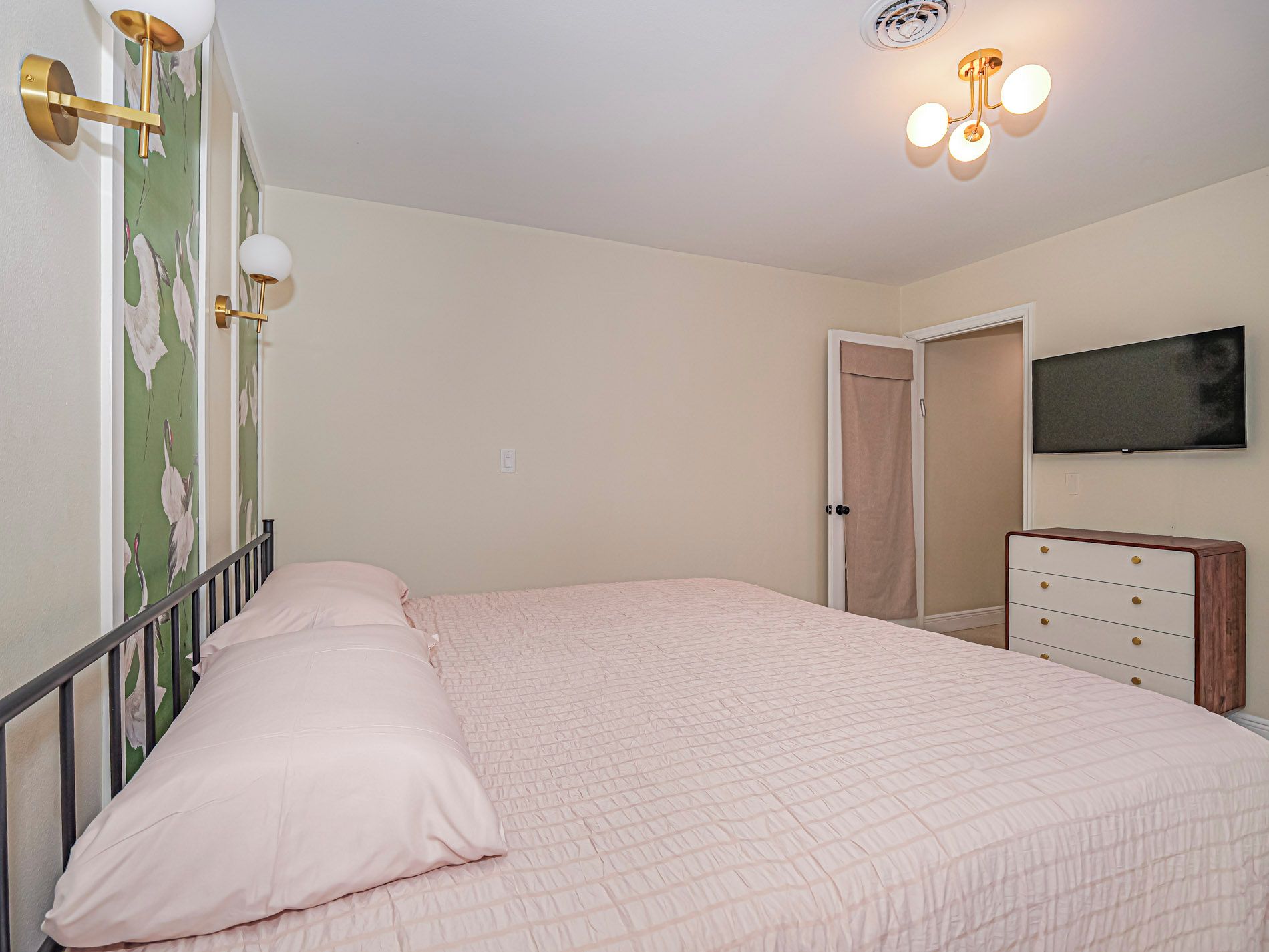 Un dormitorio con cama, cómoda, televisor y lámpara de pared.
