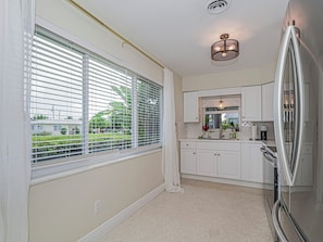 A kitchen with white cabinets, a stainless steel refrigerator, and a window with blinds.