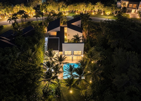 Uma casa moderna com piscina, rodeada por palmeiras.