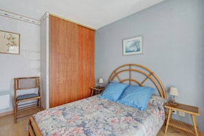 Un dormitorio con cama, armario de madera, mesita de noche, lámpara y un cuadro en la pared.