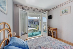A bedroom with a bed, a chair, a small table, a TV, and a balcony with a view of buildings. - Bed and Breakfast 'Chambre Jane - Chez Claudine' with Balcony and Wi-Fi (Le Teich)