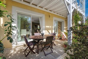 An outdoor patio with a table and chairs, a covered area with a ceiling, and a view into the house. - Bed and Breakfast 'Chambre Jane - Chez Claudine' with Balcony and Wi-Fi (Le Teich)