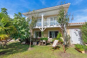 A two-story house with a balcony, surrounded by a well-maintained garden with various plants and a lawn. - Bed and Breakfast 'Chambre Jane - Chez Claudine' with Balcony and Wi-Fi (Le Teich)