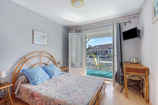 A bedroom with a bed, a desk, a chair, a TV, and a window with a view of buildings. - Bed and Breakfast 'Chambre Jane - Chez Claudine' with Balcony and Wi-Fi (Le Teich)