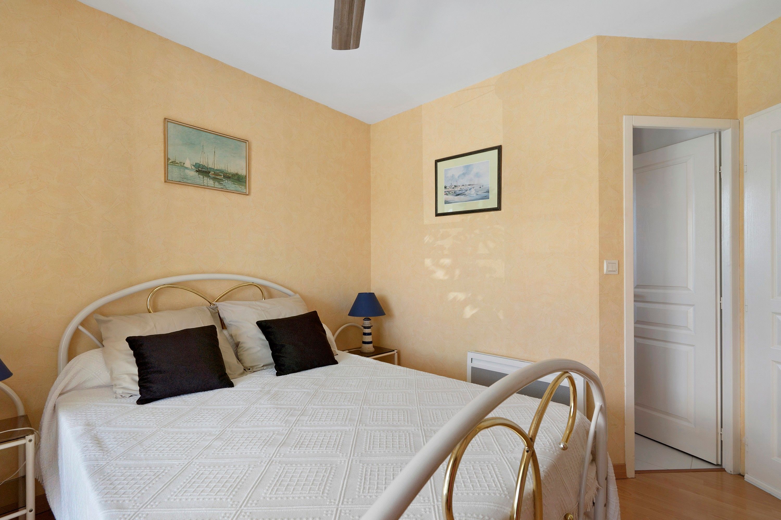 Une chambre à coucher avec un lit, deux tableaux accrochés au mur, une lampe de chevet et une porte.