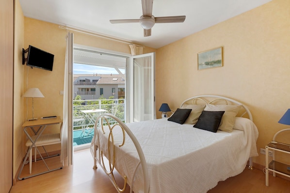 A bedroom with a bed, a television, a desk, and a balcony. - Bed and Breakfast 'Chambre Christy - Chez Claudine' with Balcony and Wi-Fi (Le Teich)