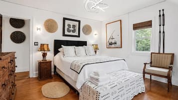 Ein Schlafzimmer mit einem Bett, Nachttischen, einem Sessel und einem Fenster mit Vorhängen.