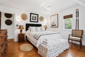 A bedroom with a bed, bedside tables, a chair, and a window with curtains. - Luangisa African House (Mount Vernon)
