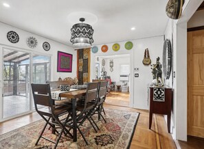 A dining area with a wooden table and chairs, a patterned rug, and a decorative wall hanging. - Luangisa African House (Mount Vernon)