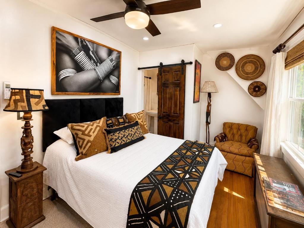 A bedroom with a bed, a chair, a desk, a ceiling fan, and wall decor.