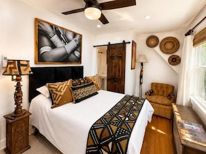 A bedroom with a bed, a chair, a desk, a ceiling fan, and wall decor. - Luangisa African House (Mount Vernon)