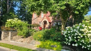 Ein Haus aus Stein mit rotem Dach, umgeben von üppigem Grün und weißen Blüten.