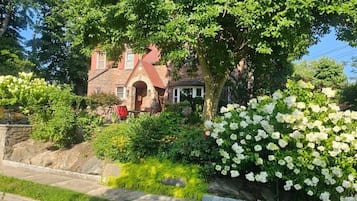 Ein Haus aus Stein mit rotem Dach, umgeben von üppigem Grün und weißen Blüten.