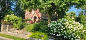 A stone house with a red roof, surrounded by lush greenery and white flowers. - Luangisa African House (Mount Vernon)