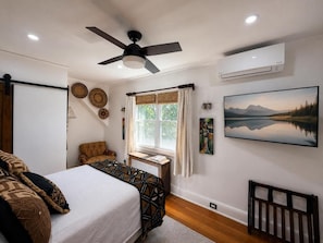 A bedroom with a bed, a chair, a desk, and a window with curtains.