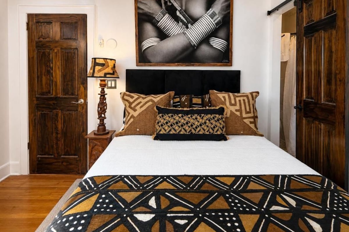 Ein Schlafzimmer mit Bett, Kopfteil, Wandgemälde, Holztür und Nachttisch mit Lampe.