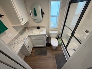 A bathroom with a white toilet, a sink, a mirror, and a window. - Magnolia MS Riverbend (Vicksburg)