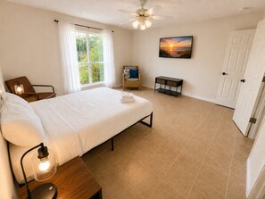 A bedroom with a bed, a chair, a desk, a ceiling fan, a window with curtains, and a door. - Crane Cove Hideaway, New Listing, Minutes to the Beach (Gulf Breeze)