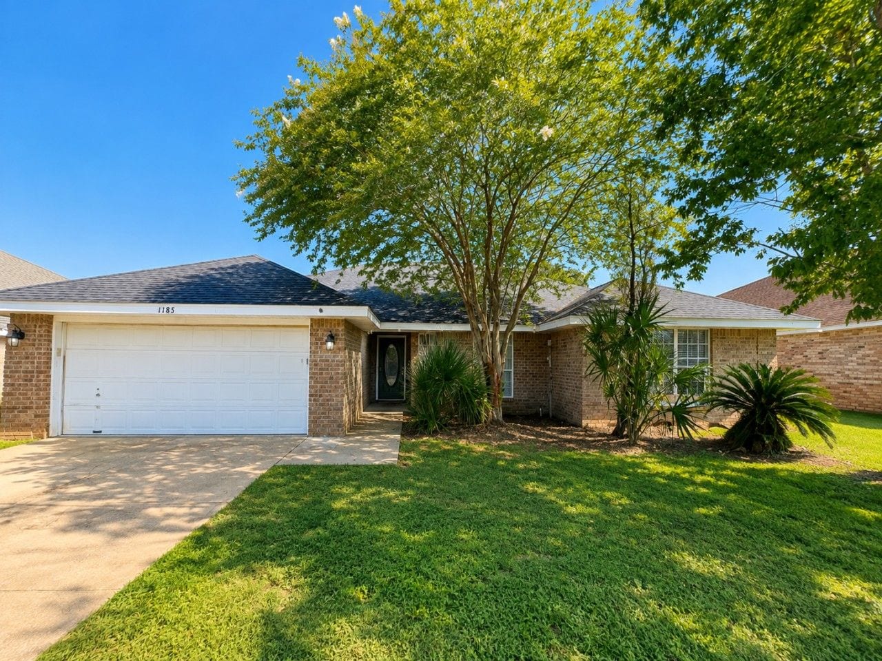 A residential house with a garage, a well-maintained lawn, and a large tree providing shade.