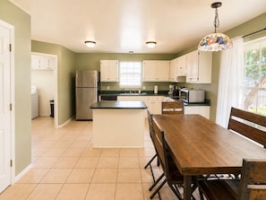 A kitchen with a central island, white cabinets, a stainless steel refrigerator, and a wooden dining table with chairs. - Crane Cove Hideaway, New Listing, Minutes to the Beach (Gulf Breeze)