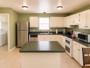 A kitchen with a central island, white cabinets, stainless steel appliances, and a window. - Crane Cove Hideaway, New Listing, Minutes to the Beach (Gulf Breeze)
