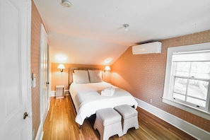 A bedroom with a bed, bedside lamps, a window, and an air conditioning unit.