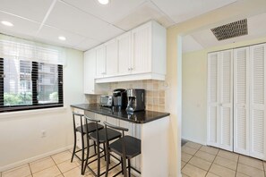 A kitchen with a central island, bar stools, a coffee maker, and a window with blinds. - Oceanfront Retreat Patio To Beach Pool Hot Tub (Hilton Head Island)