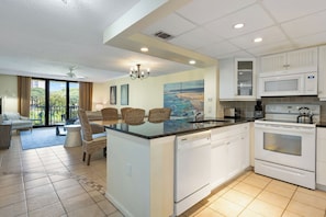 A modern kitchen with white cabinetry, a central island, and a dining area with wicker chairs. - Oceanfront Retreat Patio To Beach Pool Hot Tub (Hilton Head Island)