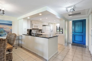 Une cuisine moderne avec des meubles blancs, un îlot central et un coin repas doté de chaises en osier.