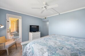 Une chambre à coucher comprenant un lit, un téléviseur, un ventilateur de plafond, une fenêtre avec des stores et une chaise.