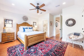 A bedroom with a wooden bed, a ceiling fan, a patterned rug, and a white door. - Resort Bungalo with Golf Cart & Beach Access (Miramar Beach)