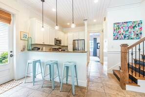 A kitchen with white cabinets, a central island with stools, a stainless steel refrigerator, and pendant lighting. - Resort Bungalo with Golf Cart & Beach Access (Miramar Beach)