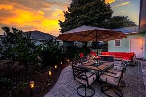An outdoor patio area with a table and chairs, a red sofa, and an umbrella. - Beach Cottage with Golf Cart & Community Pool (Destin)