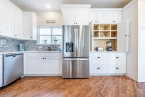 A modern kitchen with white cabinetry, a stainless steel refrigerator, a built-in water dispenser, and a wooden floor. - Beach Cottage with Golf Cart & Community Pool (Destin)