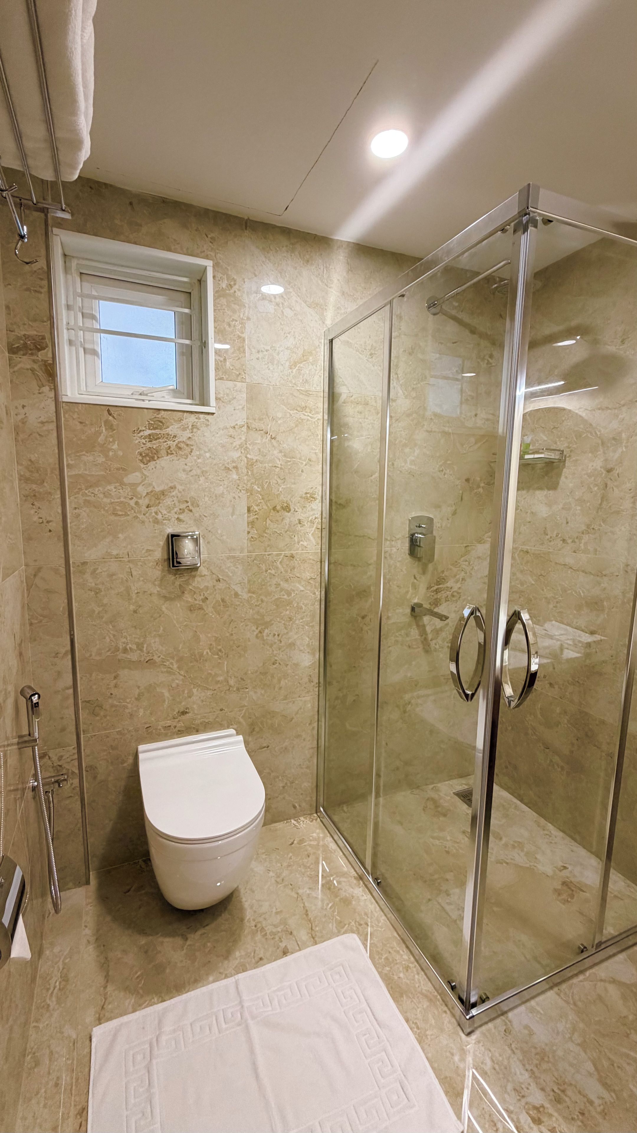A bathroom with a glass-enclosed shower, a toilet, and a towel with a geometric pattern.