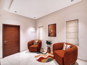 Um interior moderno com porta de madeira, dois poltronas, um tapete estampado e um quadro na parede.
